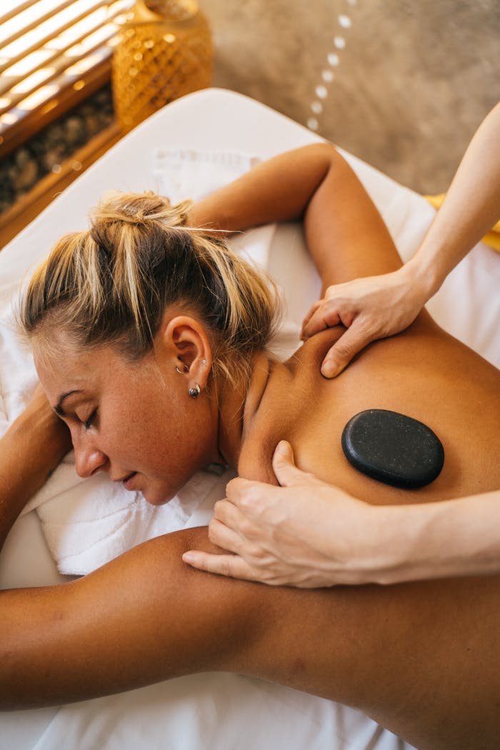 Woman enjoying a hot stone massage at a spa, promoting relaxation and pampering.